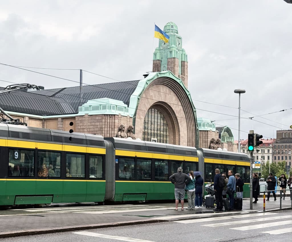 Helsinki Central Station's clock tower and stone-figure statues, Ukrainian flag flying above