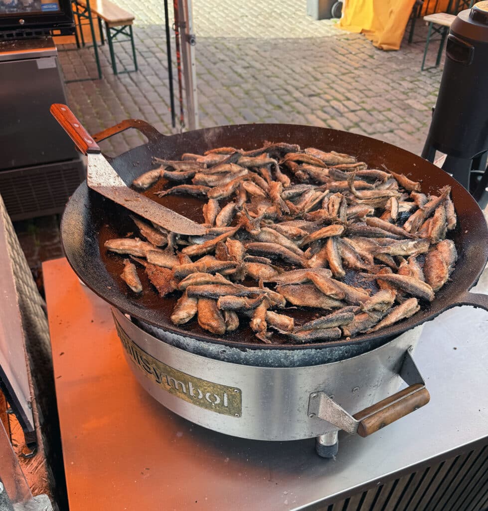 Fried vendace, a small Finnish freshwater fish, cooking on a market grill pan in Helsinki