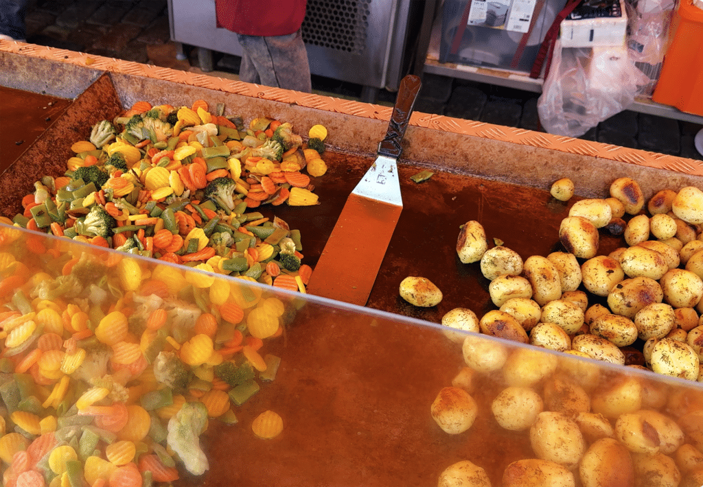 Herb-roasted potatoes and mixed vegetables cooking at a Helsinki market food stall