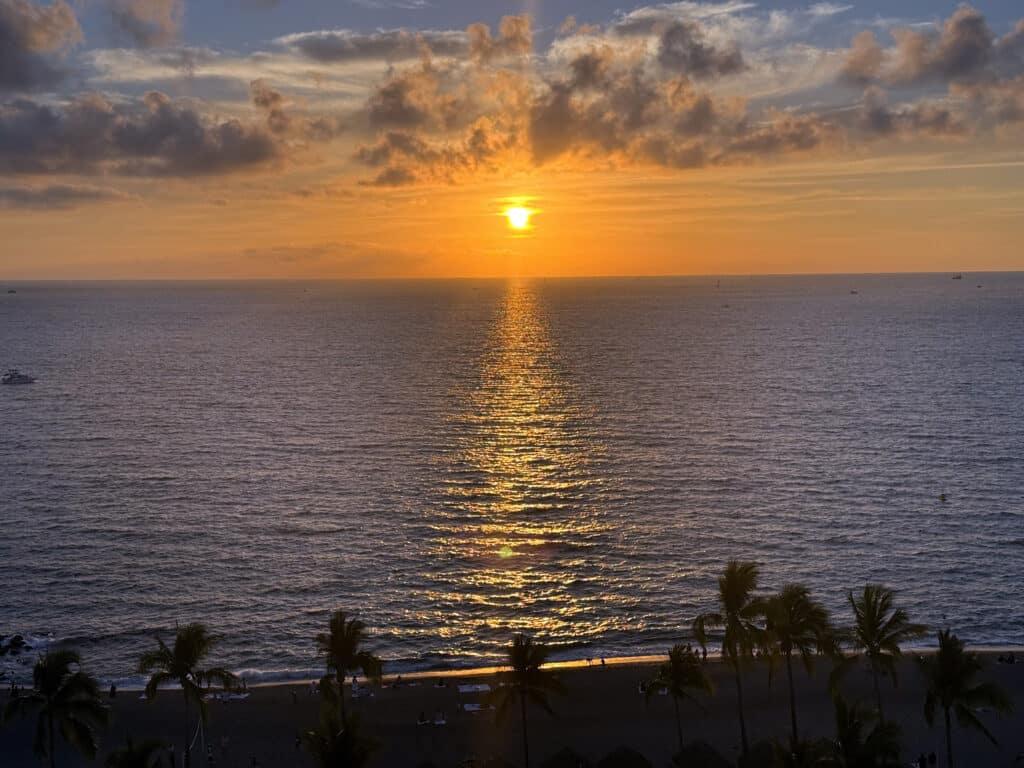 Golden sunset reflecting over the ocean water with palm trees on the beach below at Sheraton Buganvilias Puerto Vallarta.