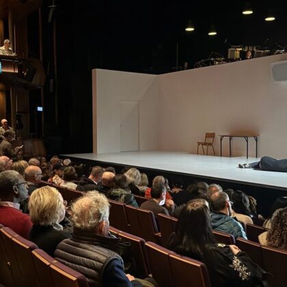 4.48 Psychosis review photo of a performer lying on a stark white stage as the Linbury Theatre audience fills the seats.