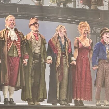 liver West End review photo of the cast bowing beneath an iron footbridge lined with Victorian lamp posts on the Gielgud Theatre stage.