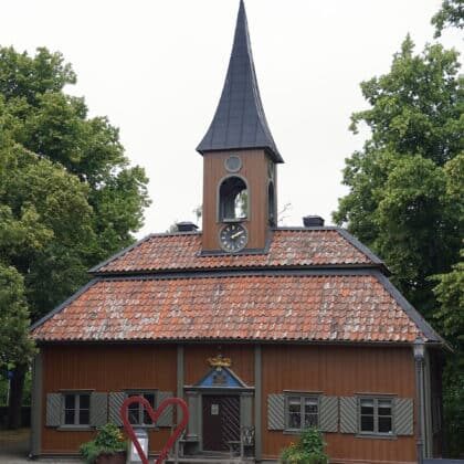 Oversized red heart sculpture in front of Sigtuna's tiny 1744 Town Hall, Swedish flags flying, gravel square in the foreground.