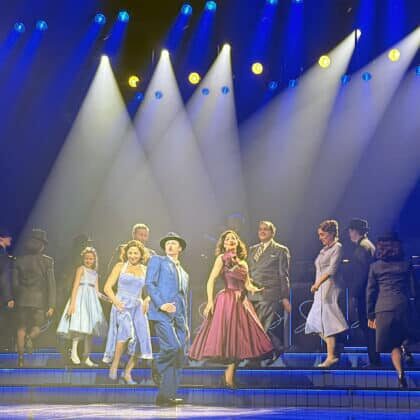 The full cast of Sinatra The Musical performing in mid-century costumes under dramatic blue spotlights on stage at London's Aldwych Theatre